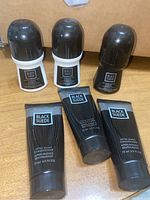 Photo showing three tubes of Black Suede After Shave Conditioner alongside three roll-on deodorants on a cardboard background.