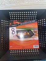 Photo showing the top view of the black non-stick wok style grill basket with label attached indicating brand, size, and product use.