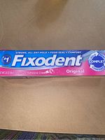 Front view of Fixodent Original denture adhesive cream tube packaging showing brand, product name, and weight (2.4 oz).
