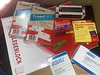Photo showing legal size notepads, Avery printed index tabs, boxes of staples, reinforcement labels, colored paper clips, and green binder clips.