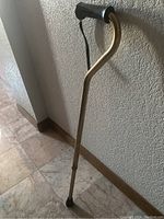 Walking cane standing on the floor showing full length and ergonomic handle with wrist strap.