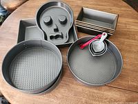 Overview photo showing all baking pans and measuring cups arranged on table, including springform pans, loaf pans, skeleton cake pan, and measuring cups.