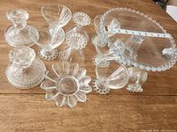 Top view of glass items on wooden table, showing the cake stand, dessert cups, flower dish, and candlestick holders with measuring tape showing 9 inches on cake stand.