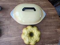 Top view of large oval roaster lid and yellow bundt cake pan with floral pattern on wooden table