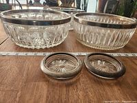 Front view of two glass bowls and two ashtrays with a measuring tape in front for scale, bowls show detailed cut glass patterns and ashtrays have silver rims.