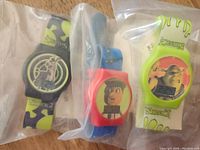 Three collectible watches featuring Shrek, Pinocchio, and another character, all sealed in plastic bags.