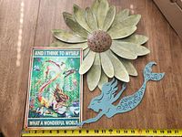 Three metal wall art pieces including a large flower, a mermaid, and a framed sign with text and underwater scene.