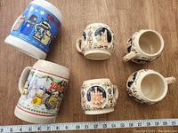 Top view of four small German steins and two larger mugs placed on wooden surface with ruler showing size.
