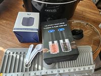 Photo of boxed electric salt and pepper mill set, boxed Mason Jar vacuum sealer, white plastic measuring spoons, and gray drain drying mat.