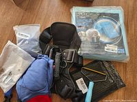 Photo showing heavy duty black XL dog harness, two pairs of blue dog pants, a metal wire hair comb, and a sealed package of underpads.