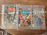 Three Marvel Star Wars comics in plastic sleeves placed on a wooden surface, titles visible include 'The Empire Strikes Back'.