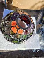 Close-up of a stained glass pendant light shade showing leaded multicolor glass pieces in orange, purple, and green with a round top opening.
