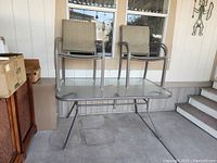 Outdoor rectangular glass top table with metal frame and four chairs stacked on top on a concrete patio.