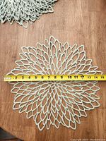 Sage green placemat with petal cutout design measured with yellow tape measure showing about 14 inches wide