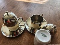Close up of the Turkish hammered silverplate espresso cups, two cups with saucers and one cup inverted showing Gural marking.