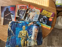 Star Wars magazines, Jar Jar Binks mug, and folded twin flat sheet with Star Wars characters C-3PO and Jar Jar Binks visible