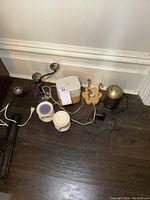 Photo showing 2 electric diffusers, 2 ceramic scent warmers with wax residue, and a metal three-arm candelabra candle holder on floor.