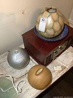 Silver metallic spherical electric diffuser with vent holes and power cord, displayed on a white surface next to a wood finish diffuser and large ceramic vase on a blue bowl