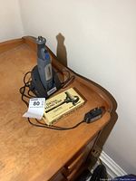 Dremel Micro rotary tool on charging station with charger and boxed detail hand vise on wooden desk.