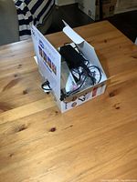 Open box displaying the contents on a wooden surface, showing the device and accessories inside.