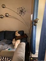 View of the tall floor lamp with five flexible chrome arms and spherical heads near a couch and window.