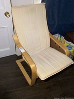 Side view of IKEA wooden framed chair with beige cushion and visible armrest and base design.