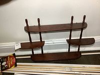 Front view of the petite wooden wall-hung knick knack shelf showing its overall shape, shelves, and hanging pegs