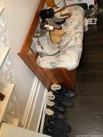 Photo showing multiple women's footwear on a bench and floor including boots, ankle boots, casual shoes mostly in tan, black and beige colors.