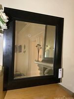 Front view of the rectangular black wood framed mirror mounted on a wall showing the reflective surface with visible discoloration and smudges.