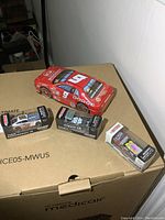 Red Dodge tin NASCAR car approximately 8 inches long alongside three sealed small diecast NASCAR cars in original boxes.