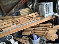 Multiple unfinished oak balusters stacked on a wooden shelf, showing square ends and turned midsections