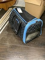 Soft sided pet carrier showing side profile, black with white diamond quilting and light blue trim on zippers and edges. Carry handles attached.