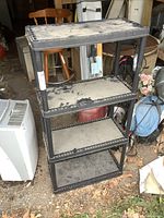 Front and side angle showing the entire four-tier resin shelving unit with dust on surfaces and surroundings showing storage area.