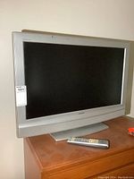 Sony 32 inch flat screen television on wooden surface with remote control beside it. Silver bezel and base stand visible.