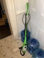 Full view of the green upright steam cleaner leaning against a wall with a cord wrapped around it.