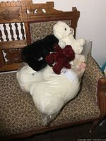 Multiple teddy bears in black, white, and maroon inside a large plastic bag placed on a patterned fabric chair.