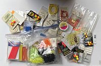 Wide view showing a large assortment of fly tying materials including beads, threads, and synthetic fibers all in plastic bags and original packaging.