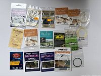 Photo showing multiple packets of fly fishing leaders and tying materials in original packaging, mostly new and sealed.