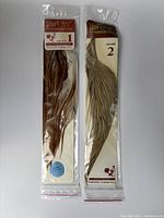 Two packs of Hoffman rooster saddle hackle feathers in original sealed packaging, showing both Grade 1 and Grade 2 labels.