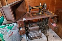 Full view of antique Singer sewing machine on wooden table with drawers and cover beside it.