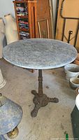 Full view of round marble top on cast iron base bistro table with surrounding items in garage.