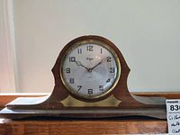 Front view of Gilbert mantel clock showing wooden case, brass bezel, and clock face with Arabic numerals.