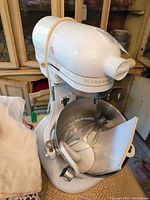 Front angle of white KitchenAid Heavy Duty stand mixer with stainless steel bowl and various attachments inside the bowl.