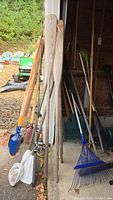 Four wood oars and two metal/plastic bars leaning against garage wall with outdoor background.