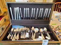 Full view of Oneida flatware set with knives, forks, spoons, and serving pieces arranged in black velvet-lined box.