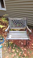 Front view of the outdoor chair showing wooden slats seat and lattice iron backrest, with cast iron armrests and legs.