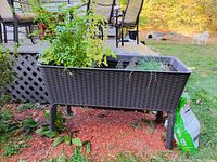 Front view of elevated plastic planter with plants and decorative stakes outdoors on mulch bed.