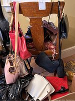 Photo showing a variety of purses and handbags hanging on and around a wooden chair, different styles and colors including red, pink, black, beige.
