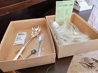 Two open boxes showing silver plate utensils, one box containing a large pierced serving fork, assorted spoons and forks in plastic wrapping, and an included checklist sheet.