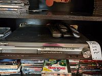 Sony DVD player with front panel showing multiple disc slots and playback control buttons, volume knob and remote controls on top.